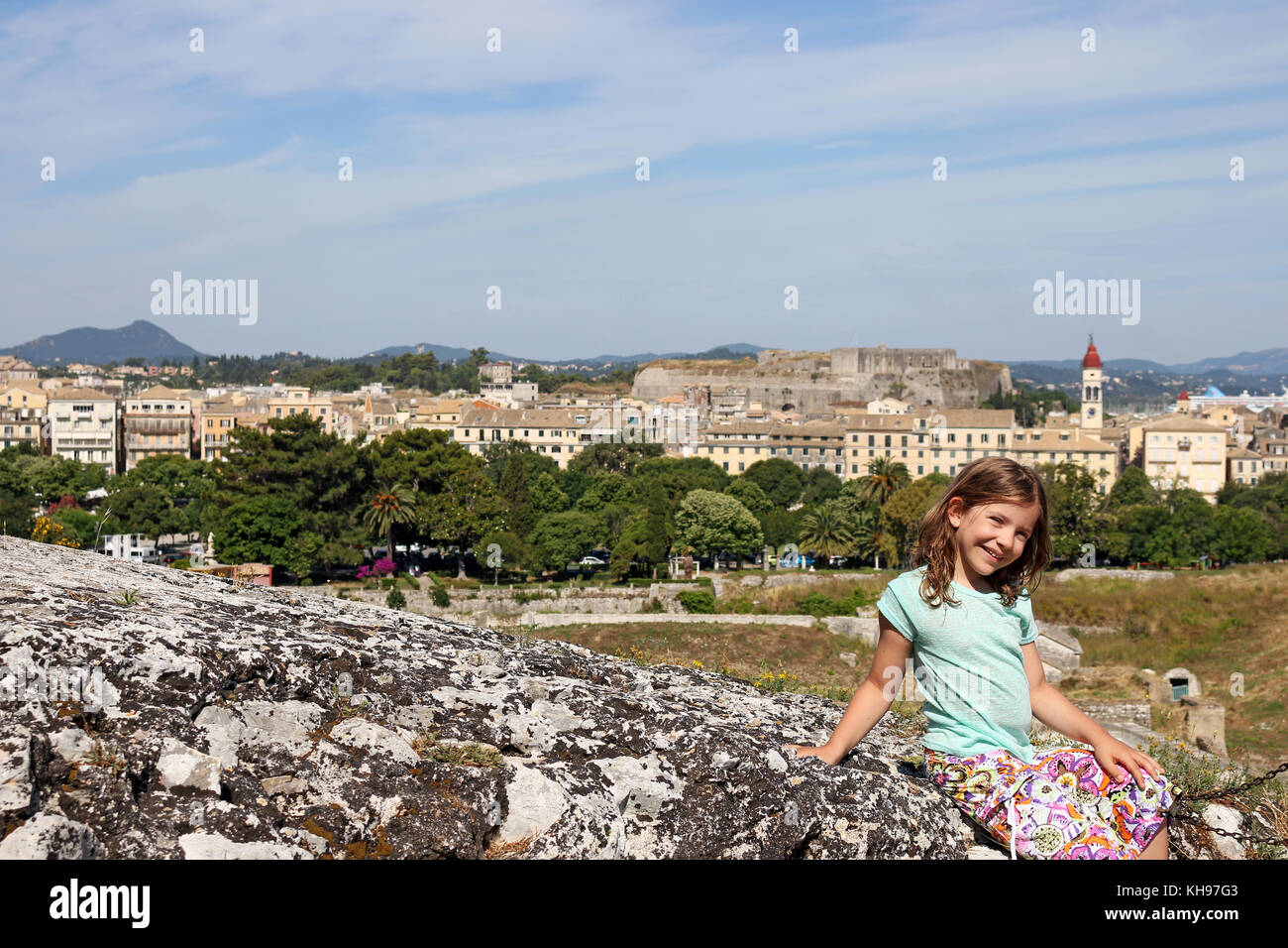 Happy little girl sitting on mur de pierre la ville de Corfou Banque D'Images