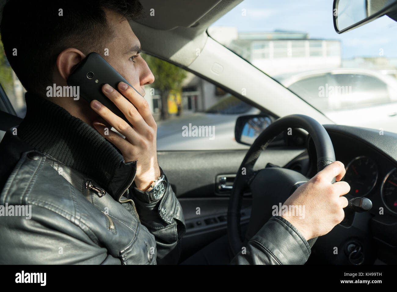 Jeune homme s'exprimant sur le téléphone portable en conduisant une voiture Banque D'Images