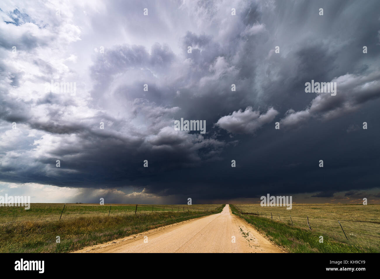 Ciel orageux avec nuages inquiétants sur un champ avec une route de terre menant à l'horizon Banque D'Images