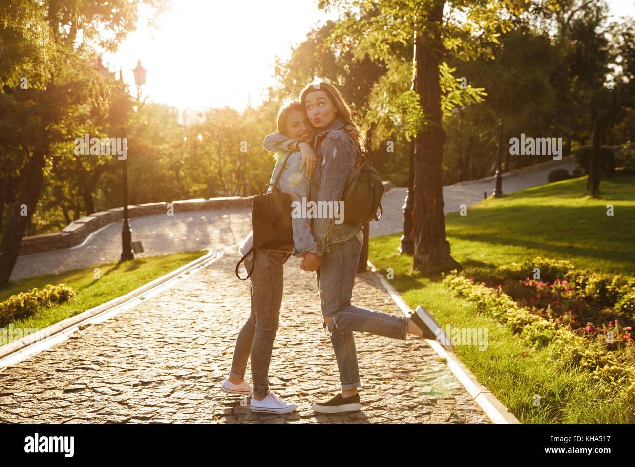 Deux heureux jeune brunette in jeans wear s'embrassent, se tenant la main tout en marchant dans le parc à l'extérieur Banque D'Images