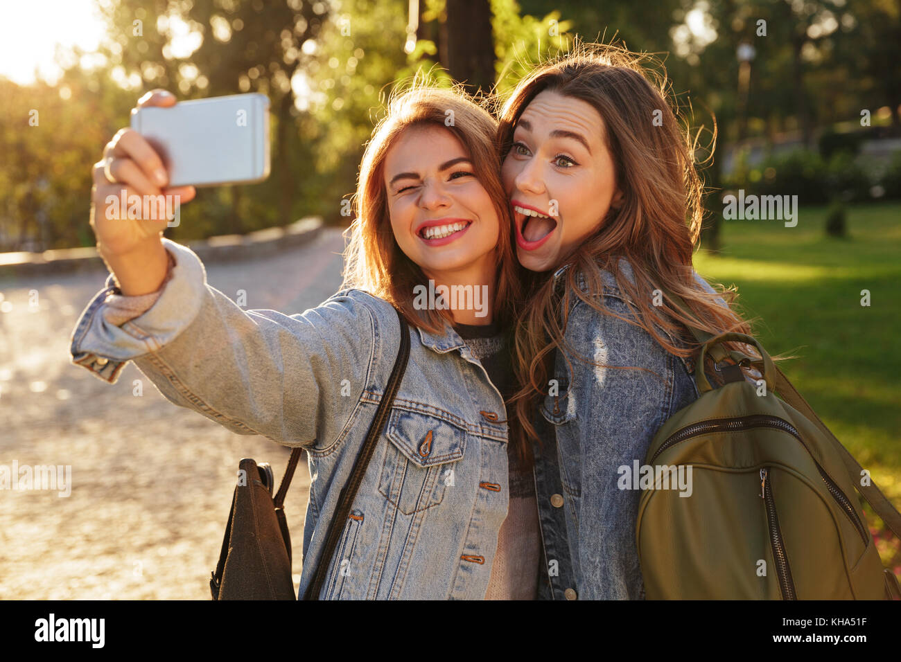 Photo en gros plan de deux filles drôle jean décontracté en faisant porter sur smartphone selfies, extérieur Banque D'Images