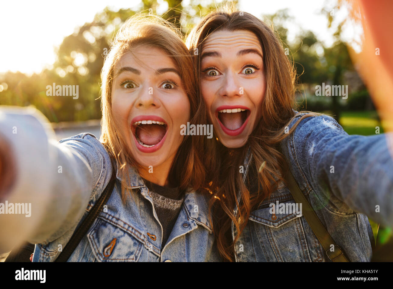 Portrait de deux jeunes filles excitées faire des grimaces tout en prenant un extérieur selfies Banque D'Images