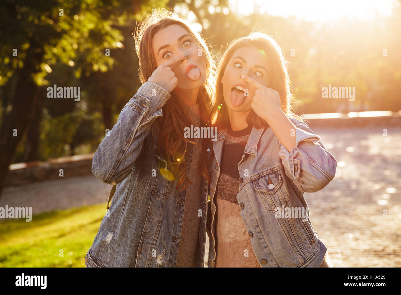 Portrait de deux jeunes filles drôle montrant langues et faire des grimaces en se tenant debout à l'extérieur Banque D'Images