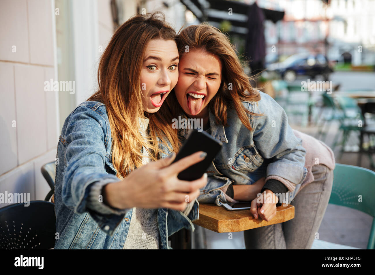 Close-up portrait of young woman drôle montrant langue maternelle tout en tenant sur selfies téléphone mobile, à l'extérieur de la ville Banque D'Images