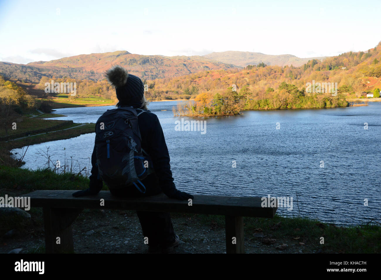 Femme tomba dans walker bobble hat assis sur banc en bois donnant sur l'eau à rydal temps d'automne dans le parc national du Lake District, Cumbria, Royaume-Uni. Banque D'Images