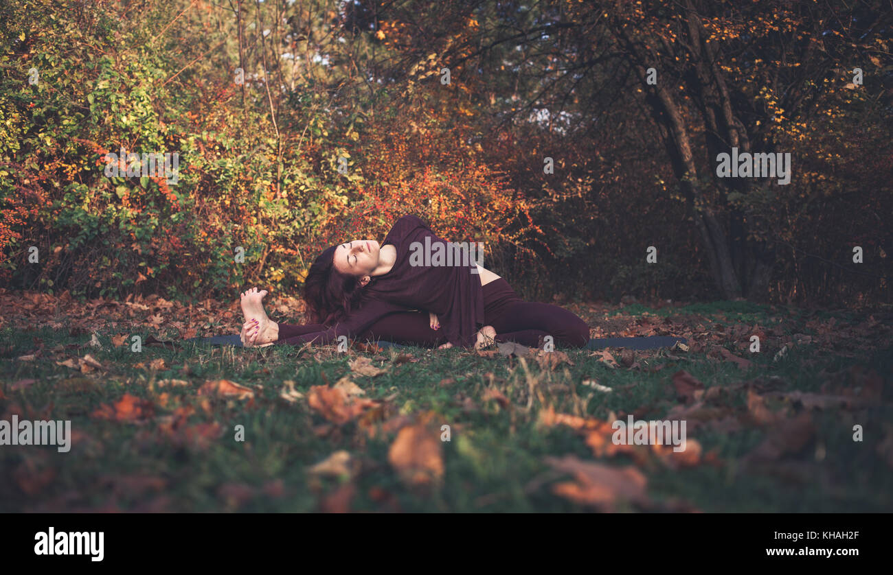 Fille sur un jour d'automne la pratique du yoga en plein air, faisant parivrtta janu sirshasana (tournait la tête-à-genou) posent, avec un bras derrière son dos Banque D'Images