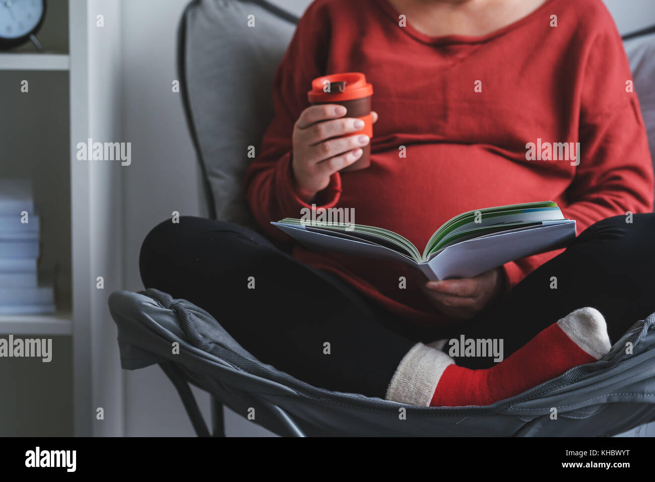 Pregnant woman reading livre sur la grossesse et la maternité dans la salle de séjour Banque D'Images