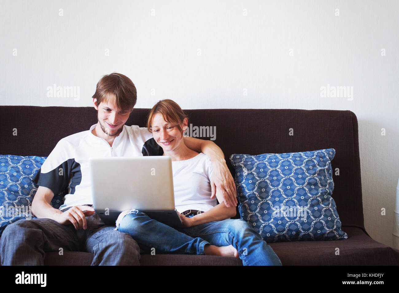 Jeune couple looking at computer et souriant, assis sur le canapé à la maison Banque D'Images
