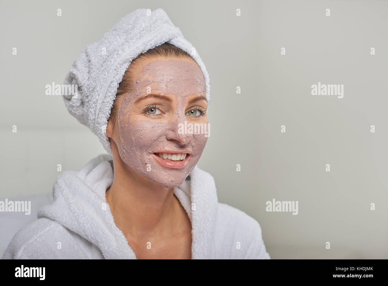 Femme dans un spa ayant un masque de beauté portant un peignoir blanc et coiffe smiling at the camera Banque D'Images