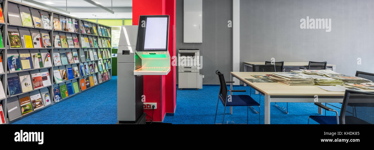 Panorama de l'intérieur de la bibliothèque avec table, chaises noires, étagères et dispositif de prêt de livres à vérification automatique Banque D'Images