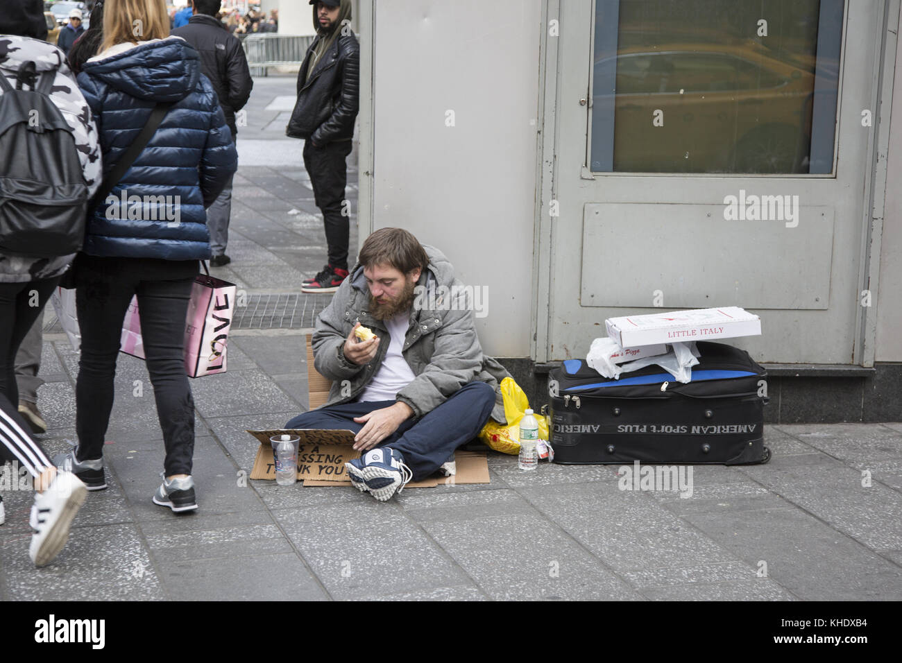 Un homme sans domicile s'assoit sur le trottoir pour demander de l'aide pendant qu'il mange une pomme dans le centre-ville de Manhattan, à New York Banque D'Images
