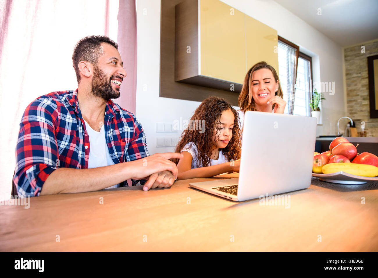 Les jeunes parents et leur fille assise à la table de la cuisine et l'aide d'un ordinateur portable Banque D'Images