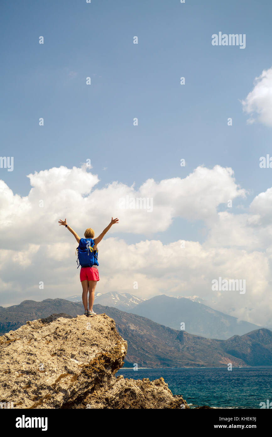 Woman with arms outstretched célébrer ou prier en inspirant lever du soleil magnifique avec les montagnes et la mer. girl la randonnée ou l'escalade avec les mains en profiter Banque D'Images