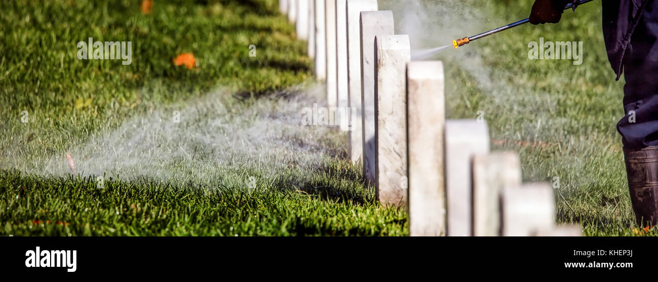 Un travailleur à un cimetière national de pierres tombales nettoyage avec un nettoyeur haute pression. Banque D'Images