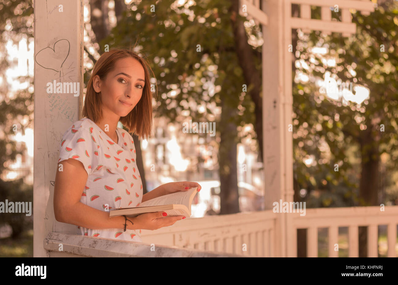 Une jeune femme lisant un livre, à l'extérieur portrait, looking at camera, journée ensoleillée Banque D'Images