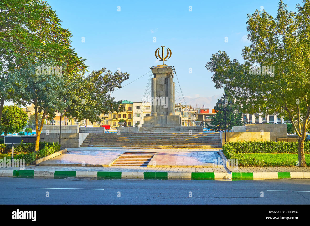 Le vert parc ombragé dans l'imam Khomeini, place agrémentée de colonnes, surmontée de l'emblème national de l'Iran (mot qu'Allah), Téhéran, Iran. Banque D'Images