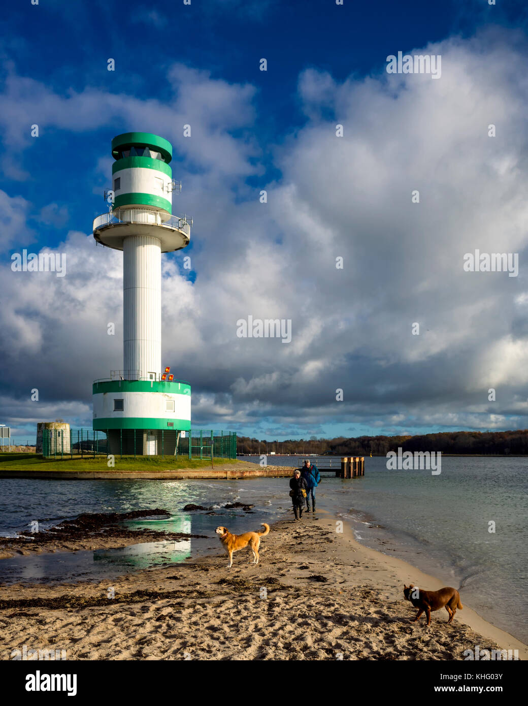 Kieler Förde, Kiel. Deutschland Allemagne. Un couple de personnes âgées promènent leurs chiens. Ils sont plus actifs à travers l'eau peu profonde à la pointe juste à côté de la plage. C'est une journée ensoleillée quelques nuages blancs près de l'horizon créer un ciel dramatique. Le pays de l'autre côté des fjords peut être vu à travers la mer à l'horizon. Banque D'Images