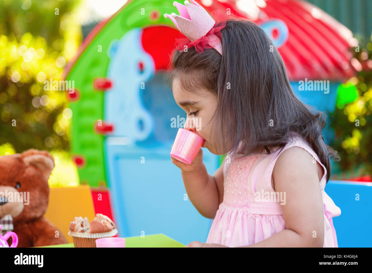 Baby girl playing tea party en plein air dans l'eau de tasse avec meilleur ami ours assis à table. robe rose et la reine ou princesse couronne Banque D'Images