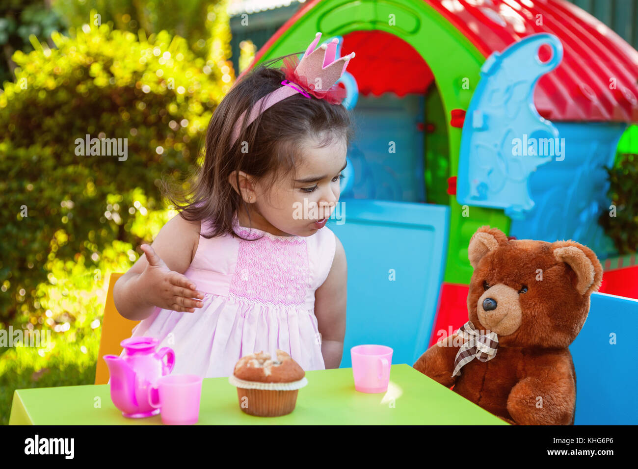 Baby girl playing in outdoor tea party parler, discuter ou partager pour son meilleur ami nounours. Robe rose et la reine ou princesse couronne. Banque D'Images