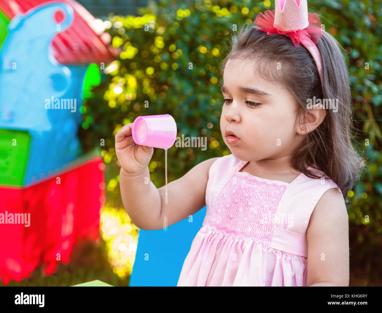 Baby girl jouant dans l'air extérieur à l'expérimentation et l'exploration en faisant un gâchis en versant le jus de tasse. robe rose et la reine ou princesse couronne Banque D'Images