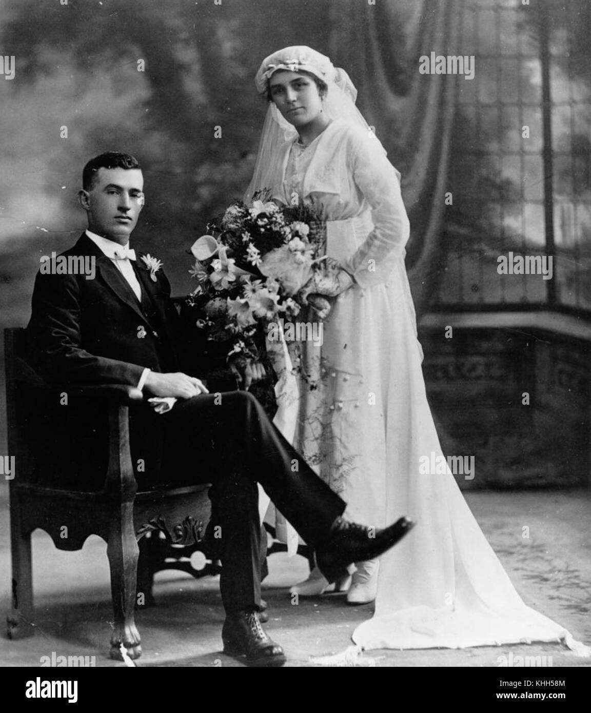 Ce portrait formel de studio capture un couple dans une photo de mariage d'environ 1910. L'image est typique de la photographie de mariage du début du XXe siècle, mettant en vedette des vêtements spécifiques à l'époque et des poses formelles. Banque D'Images