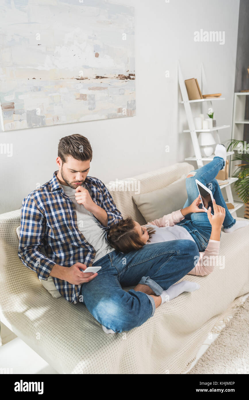 Couple sur canapé à l'aide d'appareils Banque D'Images