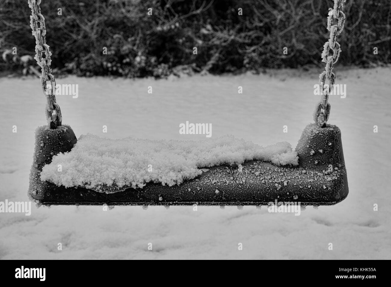 Une balançoire est recouverte de neige en partie, et des perles de glace gelée se trouvent sur les bords du siège, la chaîne chromée étant recouverte de glace le jour de l'hiver. Banque D'Images