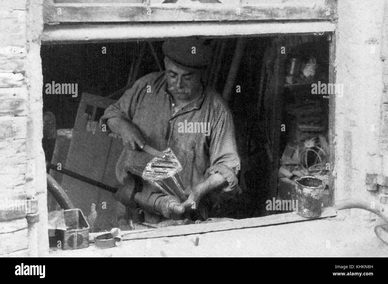Une photographie prise à travers une fenêtre d'un forgeron, identifié comme Monsieur Bonfort, il était bien connu dans la région pour la qualité de son travail, il est montré faisant une marque de bétail pour un roi du bétail dont les terres étaient loin au sud, Camargue, France, juillet 1922. Banque D'Images