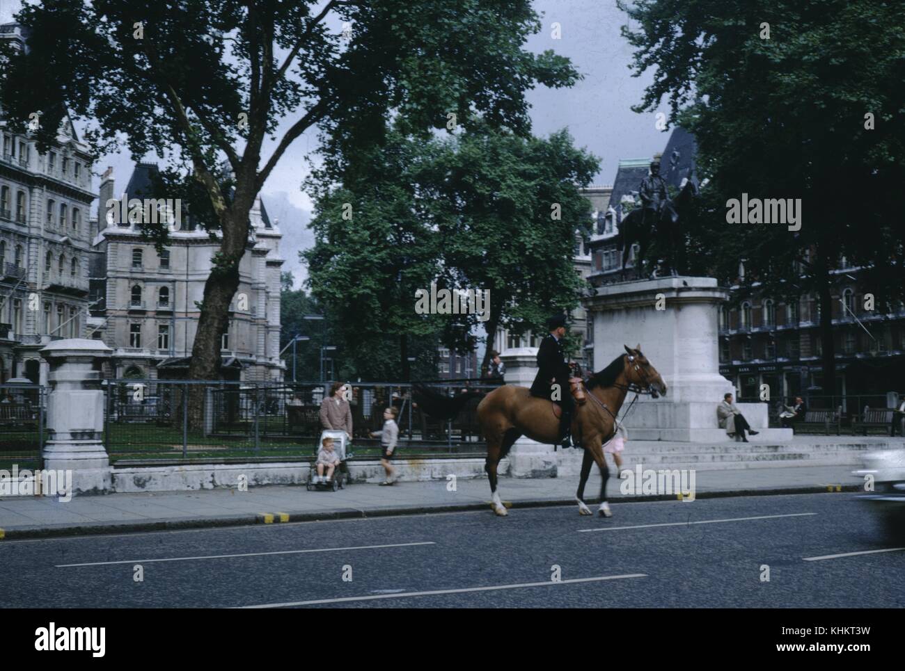 Officier de la police montée à cheval au-delà d'un parc public, une femme avec deux enfants, un dans une poussette, debout à proximité, Royaume-Uni, 1965. Banque D'Images
