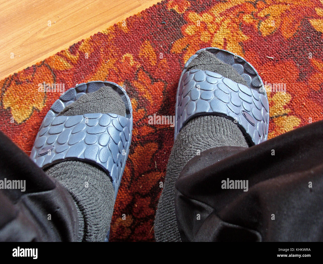 Jambes en bas de laine et des chaussons en plastique sur le tapis rouge sur le sol. Banque D'Images