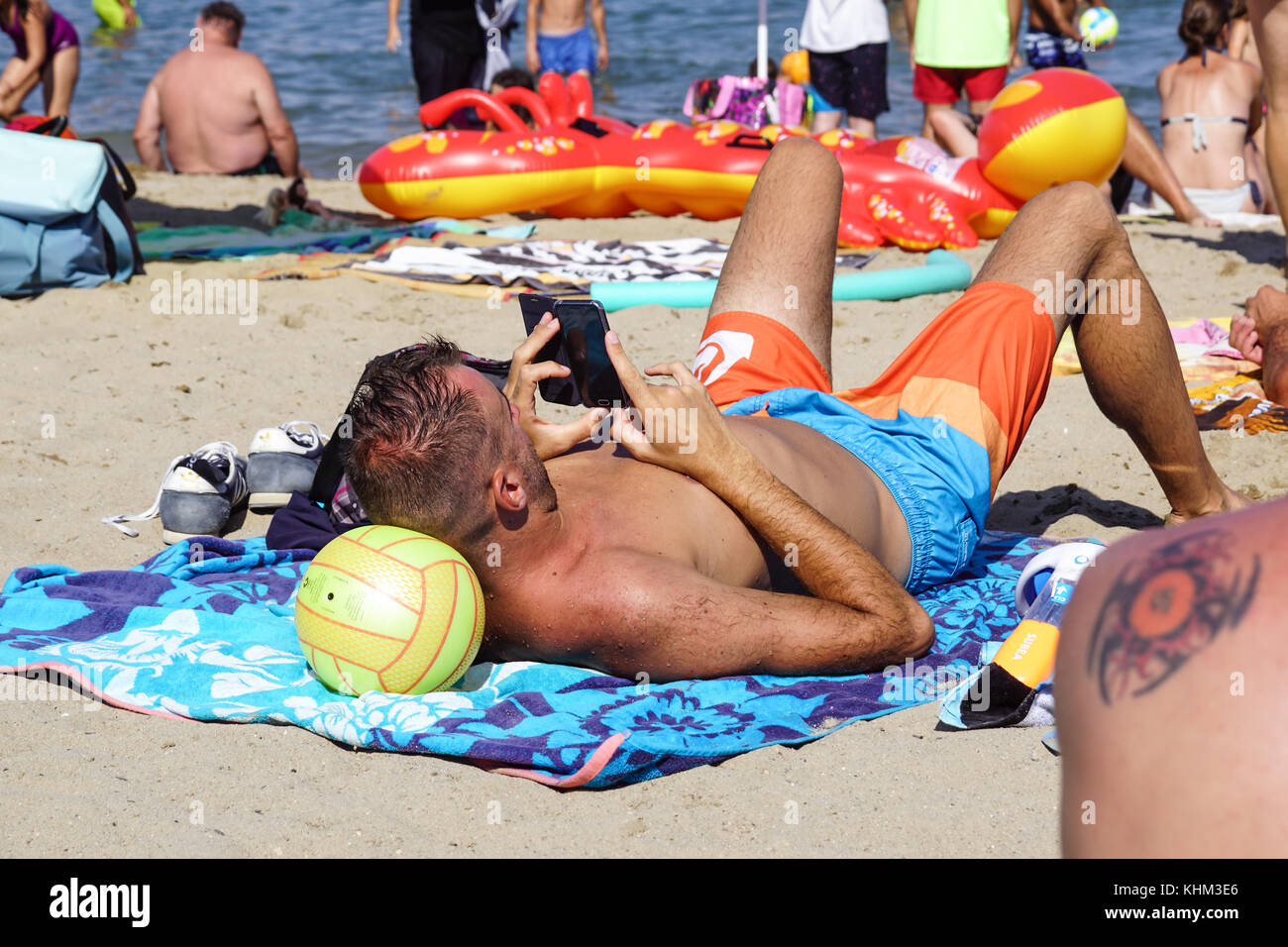 Nice , France - 5 août 2017  : vue arrière de l'homme couché reposant sur le sable et à l'aide de tablette numérique sur la plage Banque D'Images