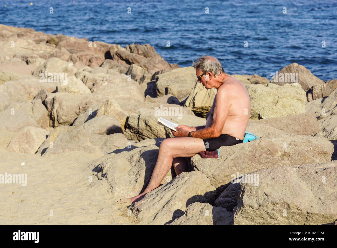 Nice , France - 5 août 2017 : vue de l'homme assis sur les rochers à se détendre et lire un livre sur la plage Banque D'Images