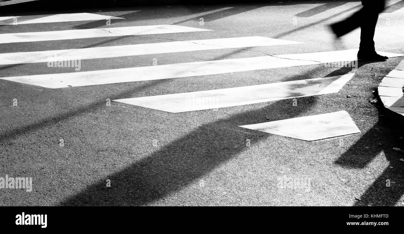 Zebra crossing floue avec silhouette et ombre de personne qui marche dans le froid et ensoleillé tôt le matin, jour d'automne en noir et blanc Banque D'Images
