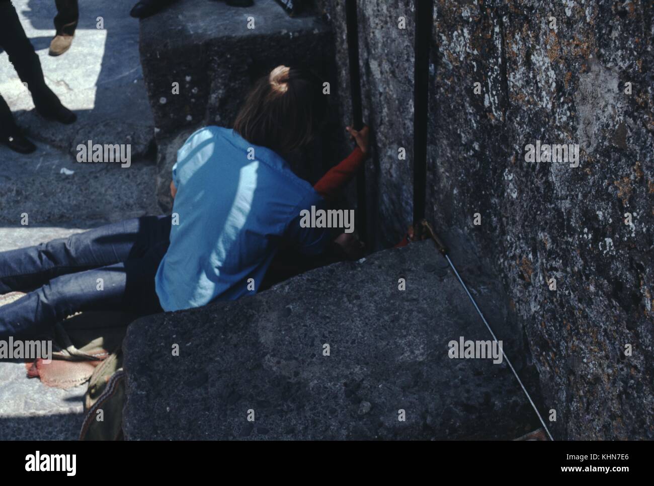 Homme couché sur le sol contre un mur de pierre, avec une femme agenouillée à côté de lui, pieds de passants visibles, 1960. Banque D'Images