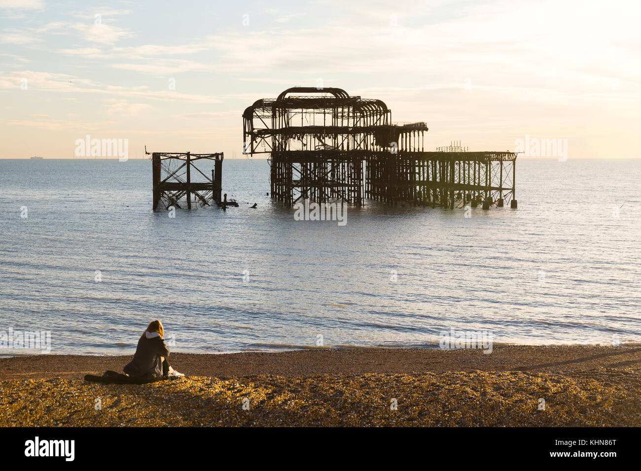 Brighton, UK. Une jeune femme regarde le coucher du soleil sur l'abandon de Brighton West Pier. Banque D'Images