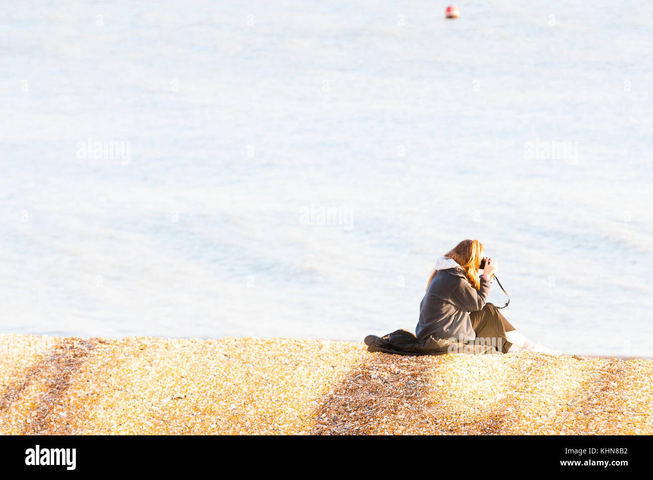 Brighton, UK. Une jeune femme est assise et prend une photo sur la plage de Brighton. Banque D'Images