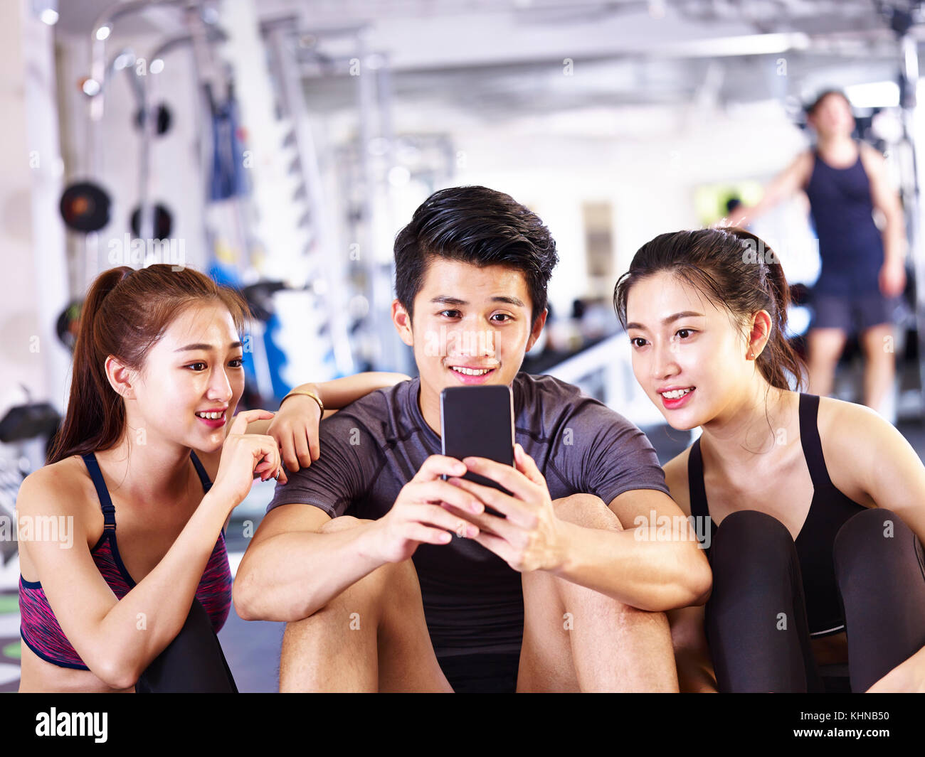 Young Asian man et les femmes à l'aide de téléphone mobile dans une salle de sport tout en faisant une pause au cours de l'exercice. Banque D'Images