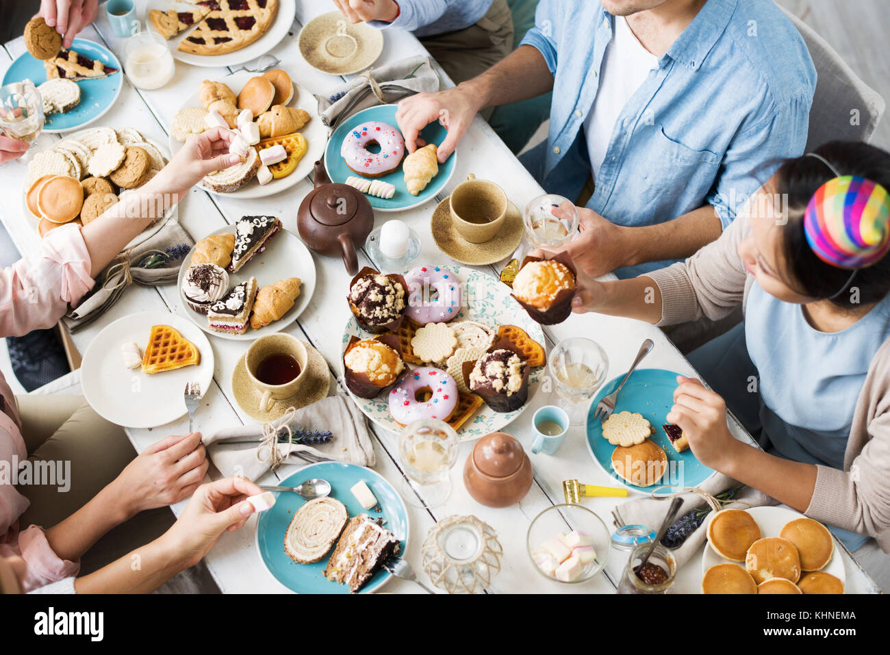 Table servie avec variété de nourriture sucrée et groupe de jeunes qui la mangent Banque D'Images