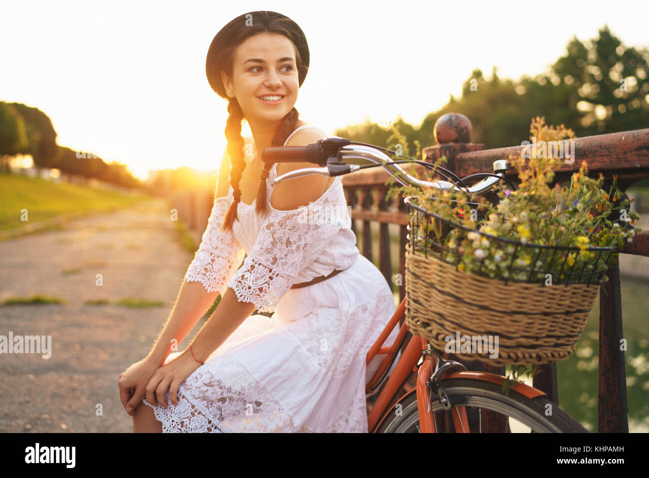 Belle Jeune femme assise sur son vélo avec des fleurs au coucher du soleil l'été et le mode de vie. Banque D'Images