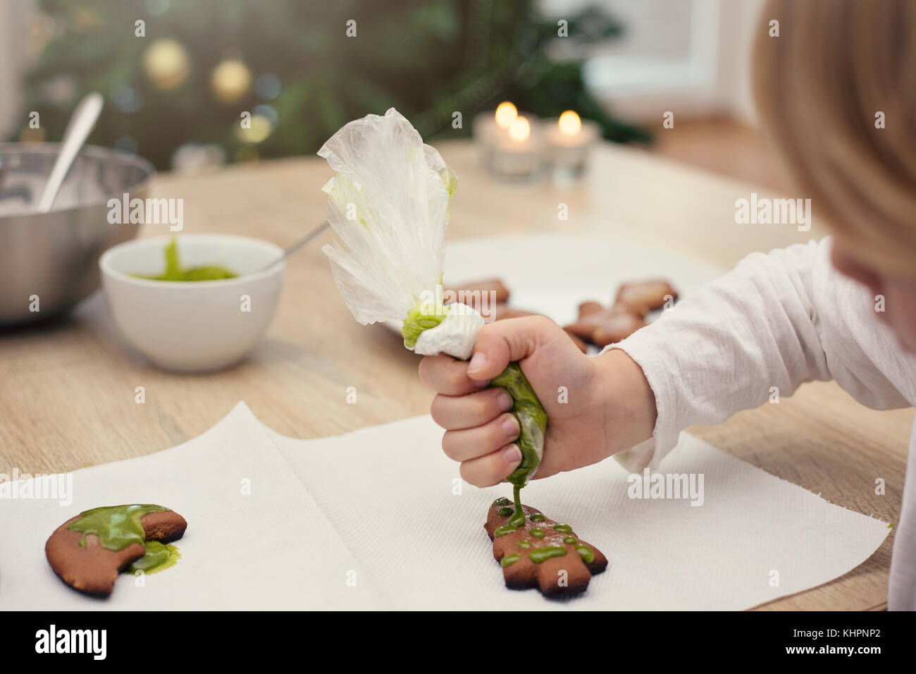 La cuisson avec les enfants, la décoration d'un petit garçon avec du pain d'épice sucre vert cerise, arbre de Noël à l'arrière-plan Banque D'Images