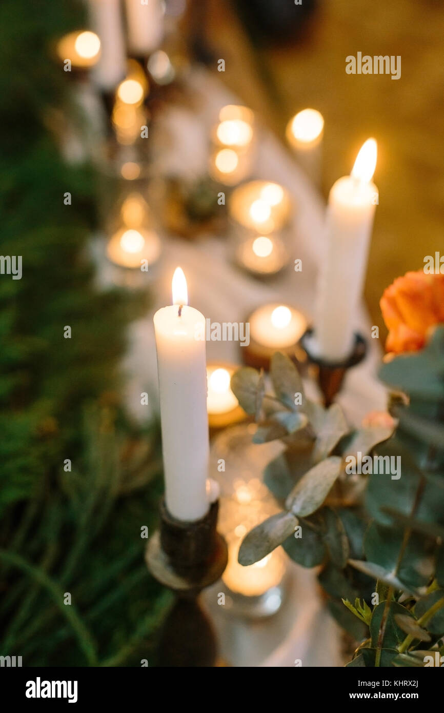Décoration de mariage, confort, concept. close up de brûler des bougies hautes dans les supports qui sont placés à proximité de roses avec brunch nuance d'orange chaud, sur le blured contexte il y a beaucoup d'éclairage Banque D'Images