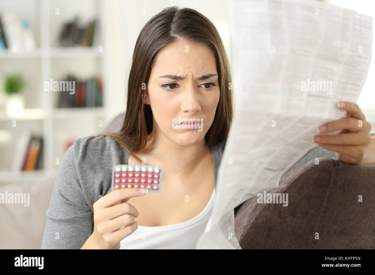 Pilules contraceptives worried woman reading leaflet assis sur un canapé à la maison Banque D'Images
