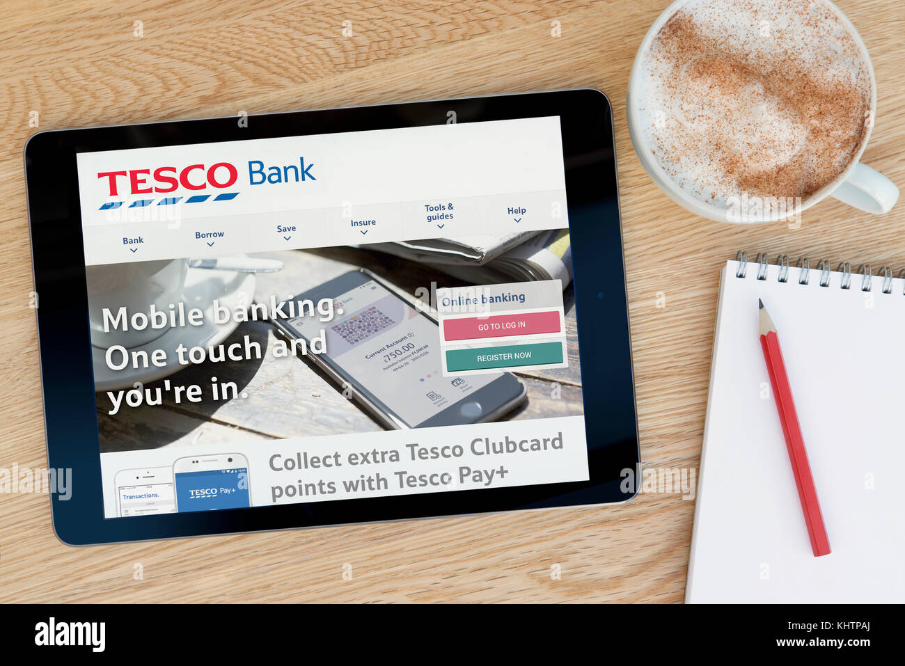Le site web de banque Tesco dispose sur un iPad tablet device qui repose sur une table en bois à côté d'un bloc-notes et un crayon et une tasse de café (seulement éditoriale Banque D'Images