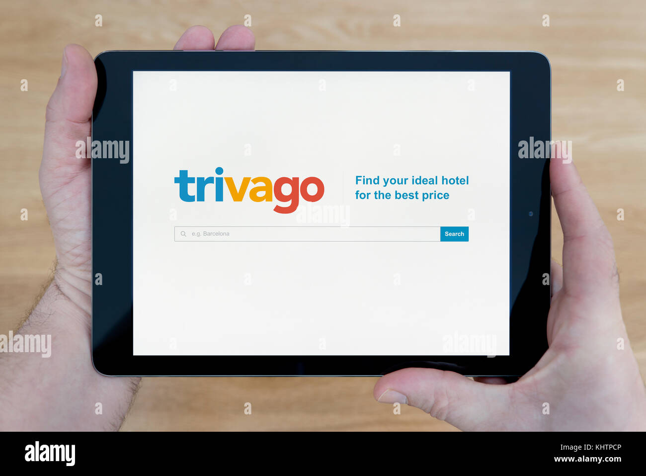 Un homme se penche sur le site Trivago sur son iPad tablet device, tourné contre une table en bois page contexte (usage éditorial uniquement) Banque D'Images