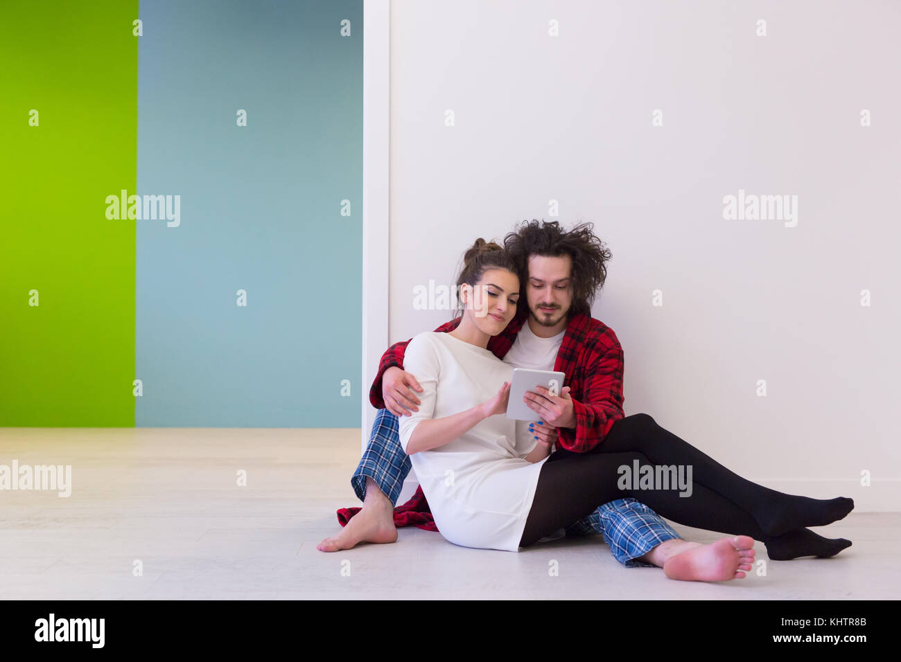 Jeune couple assis sur le plancher et à l'aide d'interent sur tablette numérique Banque D'Images
