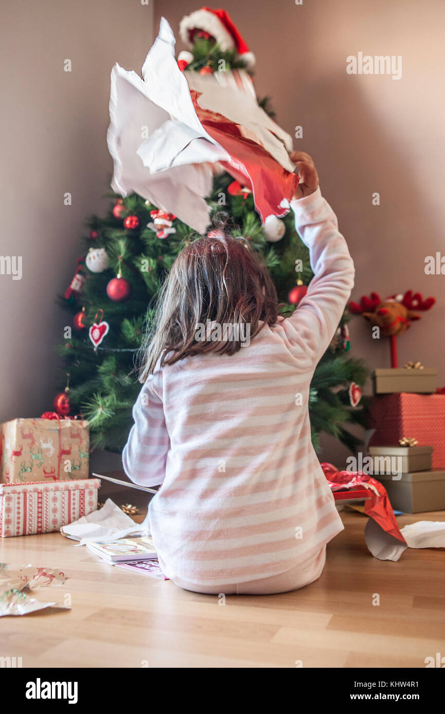 Petite fille ouvrant ses cadeaux sous l'arbre de Noël tôt le matin.Elle est éclairée par la lumière naturelle du matin Banque D'Images