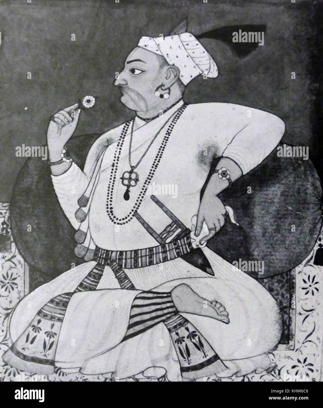 Portrait du rajah Sangram Pal de Basohli (1635-1673) assis en tailleur sur un tapis bleu et blanc ; il allongé contre une rose soutenir tout en examinant une fleur dans sa main droite, et est vêtue d'un blanc jama. En date du 18e siècle Banque D'Images