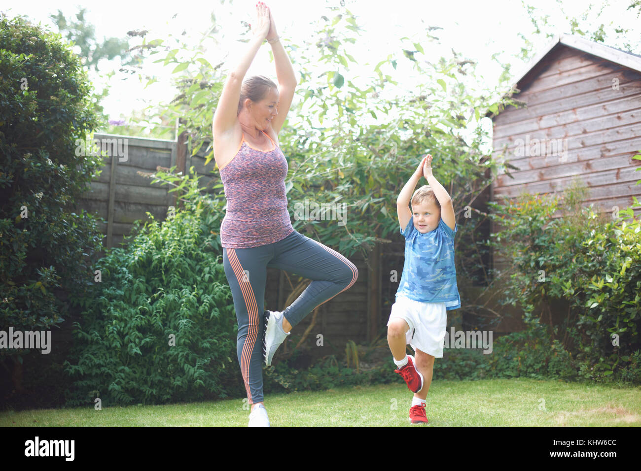 La mère et le fils dans l'exercice de jardin, debout dans la position de yoga Banque D'Images