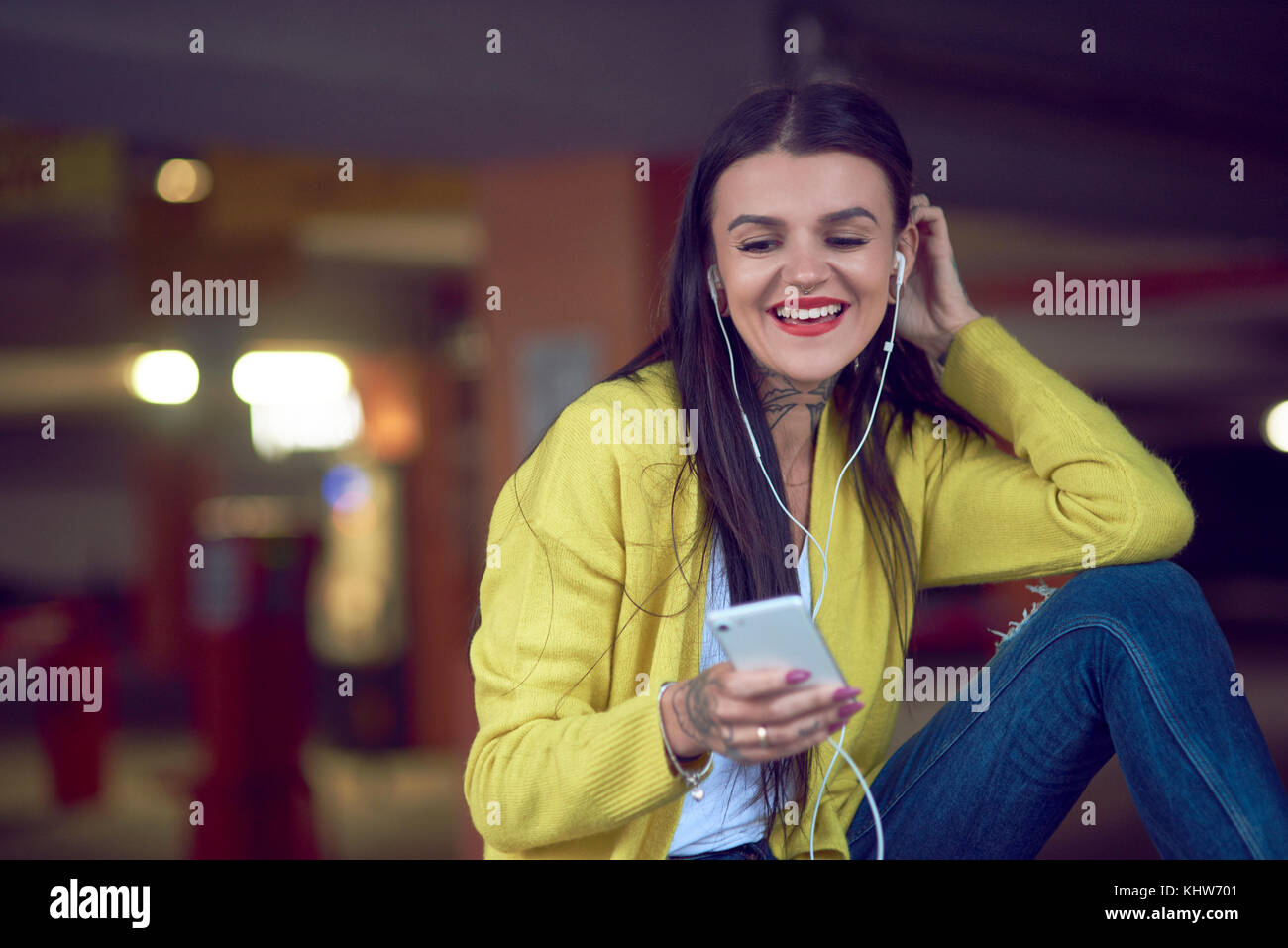 Young woman holding smartphone, wearing earphones, smiling Banque D'Images