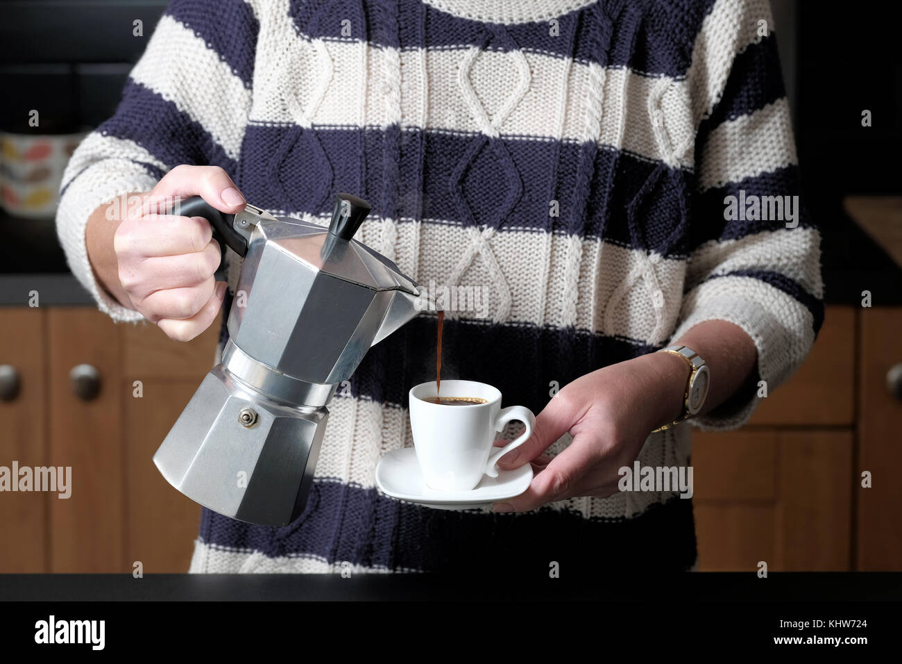 Une smart mais habillé décontracté woman pouring un café espresso à partir d'une machine à expresso cuisson molaire alors que debout dans sa cuisine à la maison Banque D'Images